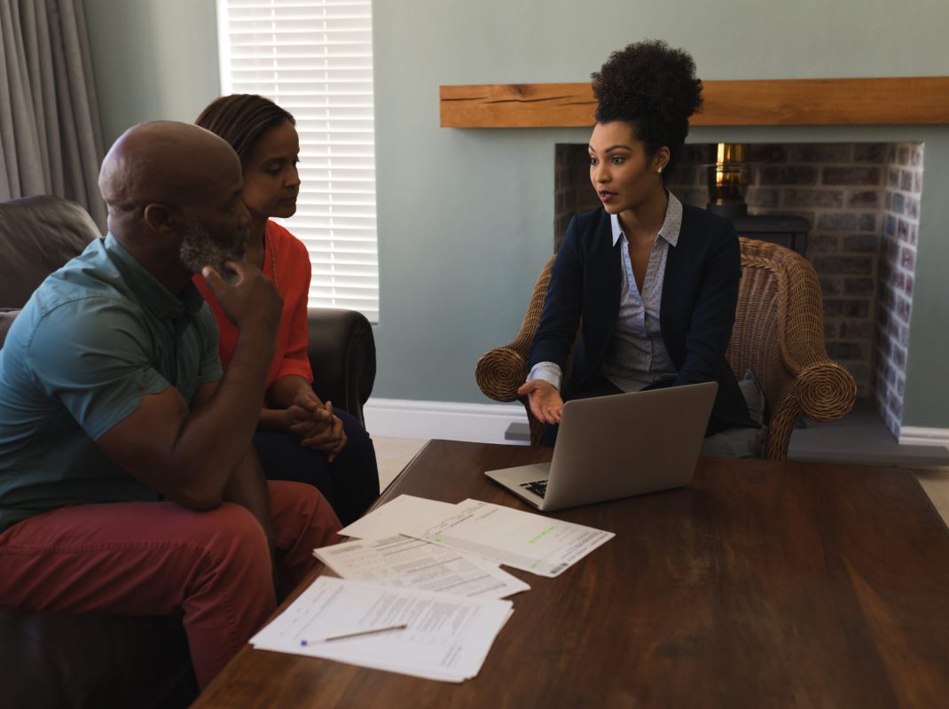 female-real-estate-agent-and-senior-couple-discuss-2023-11-27-05-12-27-utc Front view of a female real estate agent and a senior couple discussing over laptop while sitting in the living room at home